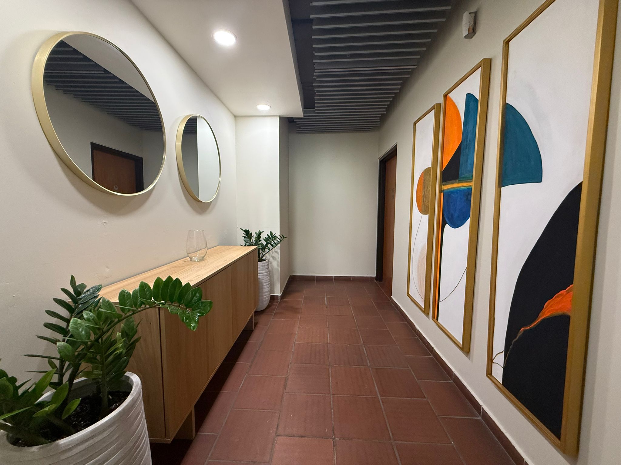 Pasillo con galeria de arte contemporaneo, espejos dorados y mobiliario de madera