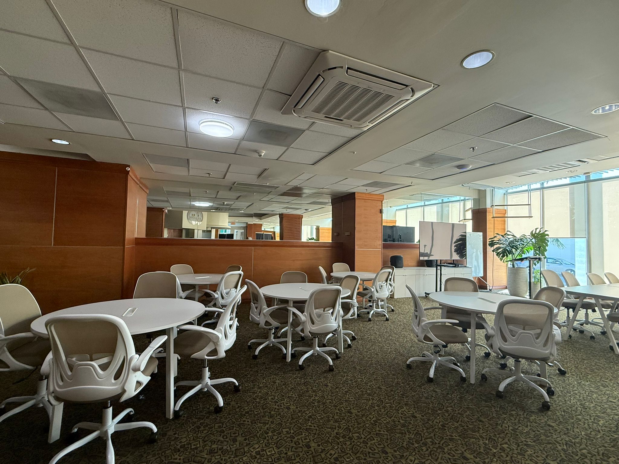 Amplia sala de trabajo colaborativo con mesas redondas, pizarra y vista panoramica